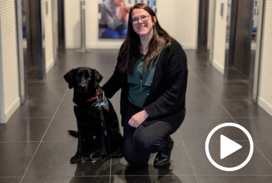 Cécile, famille d'accueil de Ualter, jeune labrador noir, se tient près de lui dans les locaux d'Amundi.