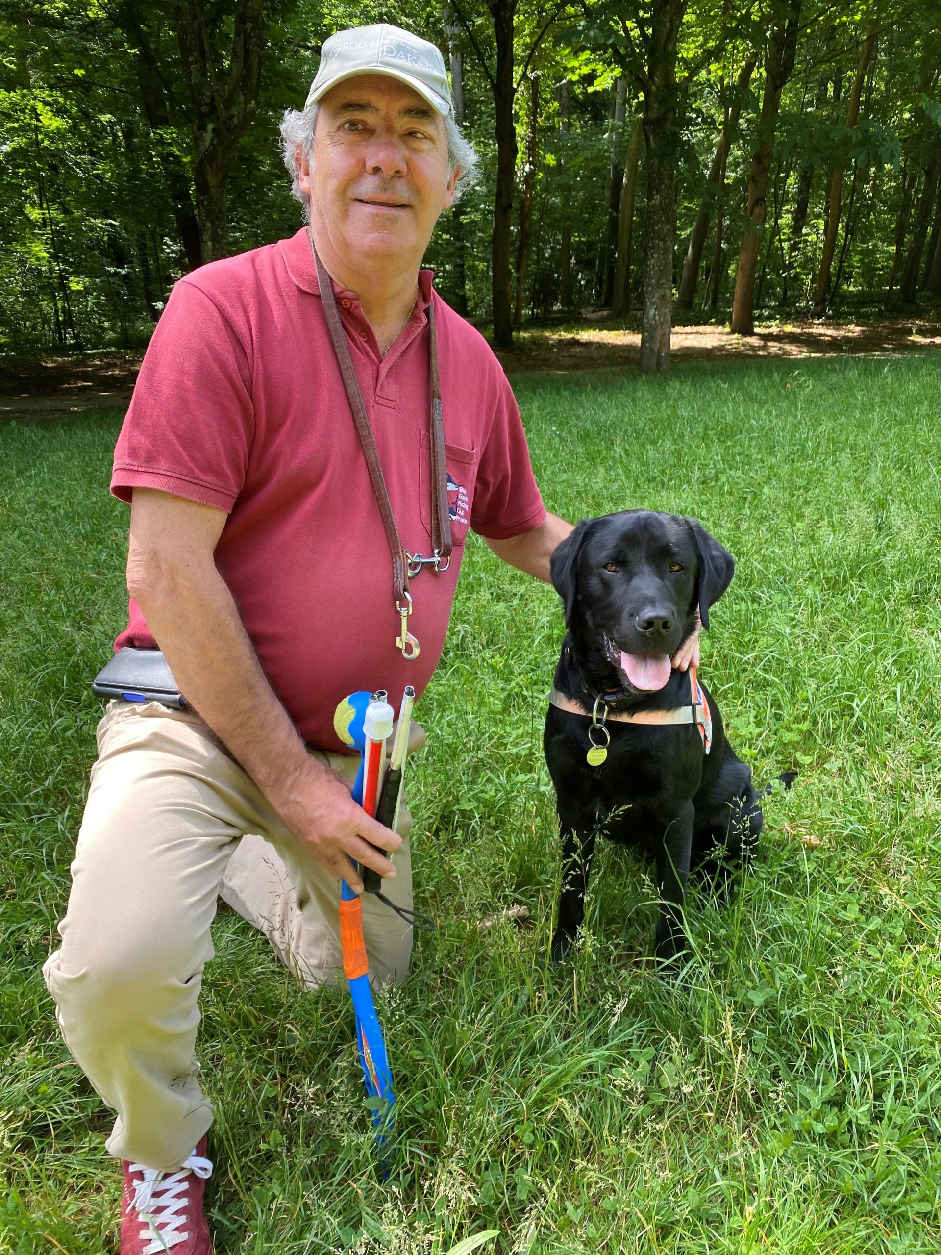 Photo de Spirit , un labrador noir assis a coté de son maitre dans l'herbe