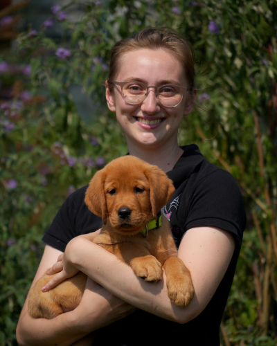 Photo d’Eline, technicienne d’élevage à Buc, tenant dans ses bras un chiot roux.